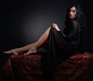 Sabahlık uzun kıvırcık saçlı Genç güzel kadın. Siyah bir arka plan üzerinde çekici esmer portresi. Kopya alanı.