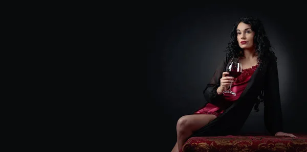 黒の背景に赤ワインのグラスと魅力的なブルネットの肖像画 ネグリジェで長い巻き毛を持つ若い美しい女性 コピー スペース — ストック写真