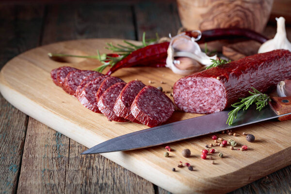 Копченая салями на старом деревянном столе. Сосиски с розмарином, чесноком и перцем.