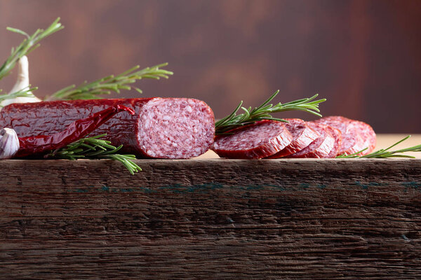 Smoked salami on a old wooden table. Sausages with rosemary , garlic and pepper. Natural wooden background. Copy space for your text.