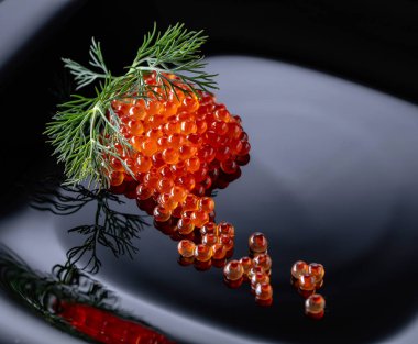 Siyah bir plaka üzerinde dereotu ile kırmızı havyar. 