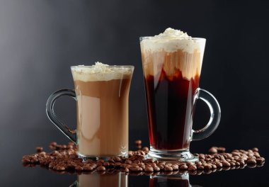 Siyah yansıtıcı arka planda çeşitli kahve içiyor. Cam bardak latte ve İrlandalı kahve.