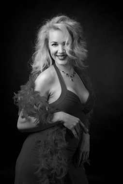 Kabarık tüy boa ile akşam elbiseli çekici orta yaş kadın. Mutlu kırk yıl sarışın siyah bir arka plan. Siyah ve beyaz.