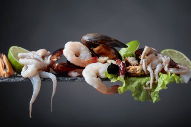 Karışık ham lezzetli deniz ürünleri Karanlık bir arka plan üzerine kireç dilimleri ile. Küçük ahtapot, karides ve midye salata yaprağı üzerinde. Akdeniz mutfak, sağlıklı organik gıda.