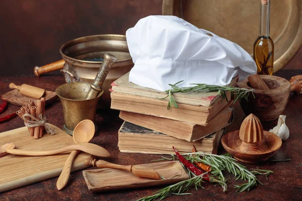 白色主厨的帽子和旧食谱 厨房用具与香料和迷迭香在餐桌上 — 图库照片