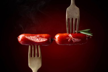 Rosemary bir çatal ile ızgara sosis. Koyu kırmızı arka plan, kopya alanı. 