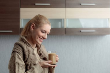 Yakın çekim portre orta yaş kadın güzel bir fincan kahve ile. Çekici ve mutlu sarışın kazaklı sütlü kahve içer. Kopya alanı.