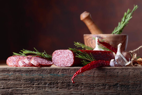 Smoked salami on a old wooden table. Sausages with rosemary , garlic and pepper. Natural wooden background. Copy space for your text.