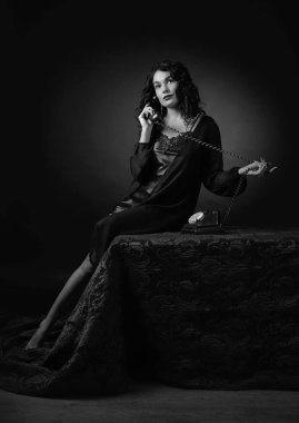 Sabahlık uzun kıvırcık saçlı Genç güzel kadın. Eski telefon ile çekici esmer portresi. Siyah ve beyaz.