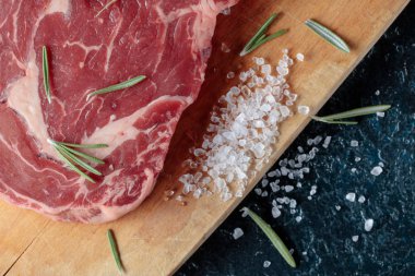 Taze çiğ Dana biftek biberiye ve deniz ile ahşap tahta üzerinde tuz. Üstten görünüm.