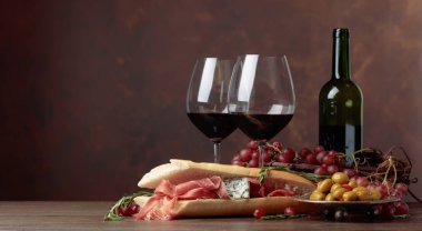 Prosciutto, mavi peynir ve koyu arkaplanda biberiyeli sandviç. Lezzetli aperatif ve kırmızı şarap. Metnin için boşluk kopyala.