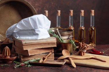 Beyaz şefin şapka ve eski yemek kitapları. Mutfak gereçleri ile şişe zeytinyağı, baharat ve biberiye mutfak masasında.