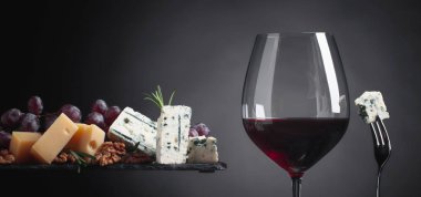 Çeşitli peynirler, üzüm, ceviz ve biberiye karanlık bir arka plan üzerinde kırmızı şarap bir bardak. Kopya alanı .