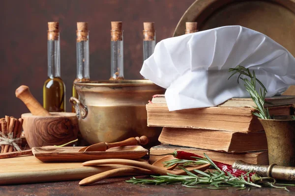 白厨的帽子和旧食谱 厨房用具 厨房桌子上有几瓶橄榄油 香料和迷迭香 — 图库照片