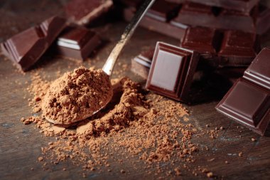 Kırık çikolata parçaları ve ahşap arka plan üzerinde küçük kaşık kakao tozu.