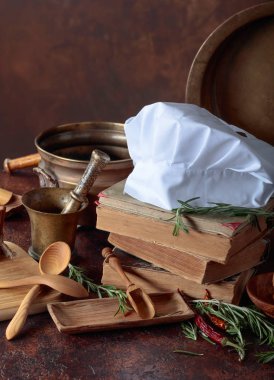 Beyaz şefin şapka ve eski yemek kitapları. Baharat ve mutfak masasında biberiye ile mutfak eşyaları.