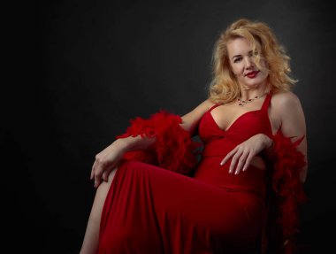 Kabarık tüy boa ile kırmızı akşam elbiseli çekici orta yaş kadın. Mutlu kırk yıl sarışın siyah bir arka plan. Kopya alanı.