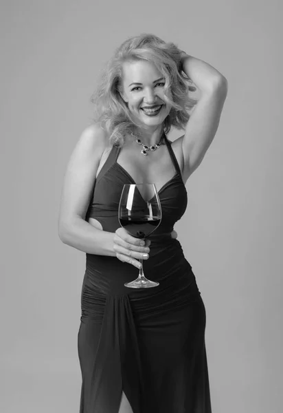 Attractive middle age woman in red evening dress with glass of red wine. Happy forty years blonde on a white background.