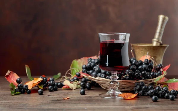 成熟黑 Chokeberry 黑楸楸 的新鲜果汁在玻璃和浆果与叶子在木背景 — 图库照片