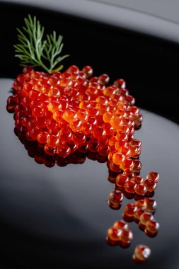 Kırmızı havyar siyah bir plaka üzerinde dereotu ile. Seçici odak.