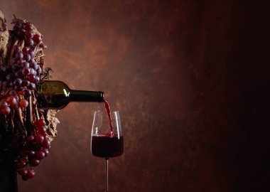 Kırmızı şarap şişeden bardağa dökülüyor. Üzümlü, sulu bir çelenk. Şarap yapımının teması üzerine kavramsal görüntü. Metnin için boşluk kopyala.