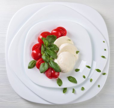 Beyaz tabakta domates ve yeşil Fesleğenli Mozzarella peyniri. Sağlıklı organik gıda.