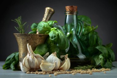 Ahşap bir masaya pesto yapmak için malzemeler. Zeytinyağı, sarımsak, Yeşil fesleğen ve çam fıstığı eski pirinç havan topu .