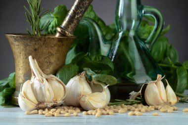 Ahşap bir masaya pesto yapmak için malzemeler. Zeytinyağı, sarımsak, Yeşil fesleğen ve çam fıstığı eski pirinç havan topu .