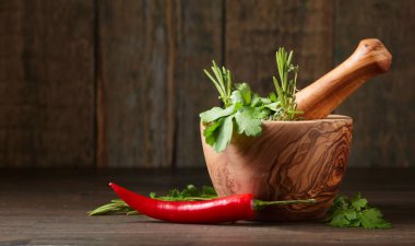 Eski ahşap bir masa üzerinde farklı otlar. Biberiye, kişniş, kekik ve maydanoz ile ahşap harç.