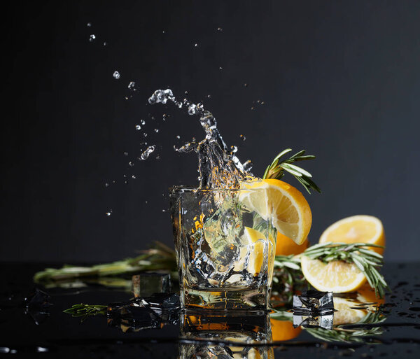 Cocktail gin-tonic with lemon slices and twigs of rosemary. Lemon slice falls into the glass. Copy space.