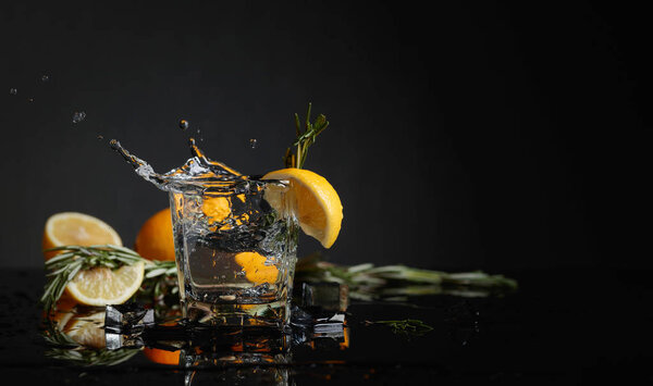 Cocktail gin-tonic with lemon slices and twigs of rosemary. Piece of ice falls into the glass. Copy space.