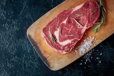 Taze çiğ Dana biftek biberiye ve deniz ile ahşap tahta üzerinde tuz. Üstten görünüm.