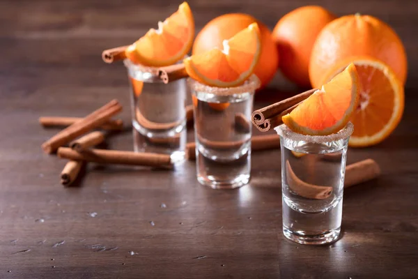 Glazen tequila met stukjes sinaasappel en kaneel stokjes . — Stockfoto