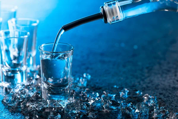 Vodka derramado em um copo iluminado com luz de fundo azul . — Fotografia de Stock