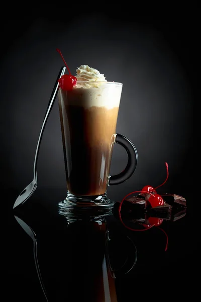 Layered coffee cocktail with whipped cream, cherry and pieces of