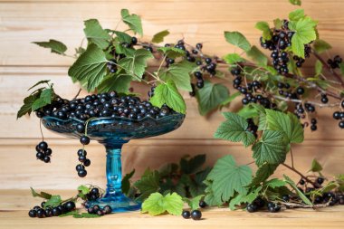 Ahşap arka plan üzerinde yaprakları ile taze olgun siyah kuş üzümü.