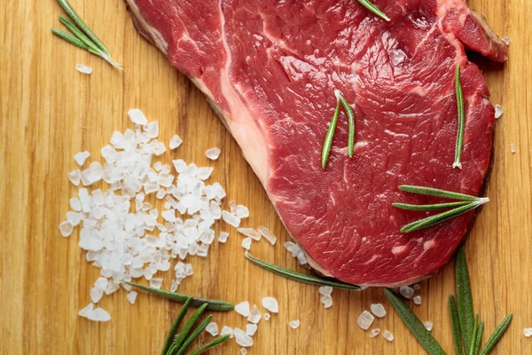 Carne fresca de res cruda sobre tabla de madera con romero y sal marina . —  Fotos de Stock