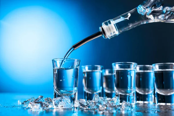 Vodka vertido en un vidrio iluminado con luz de fondo azul . — Foto de Stock