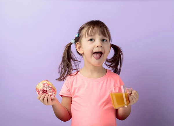 Négy-év-régi lány rózsaszín póló enni a fánk, és ital gyümölcslé. — Stock Fotó