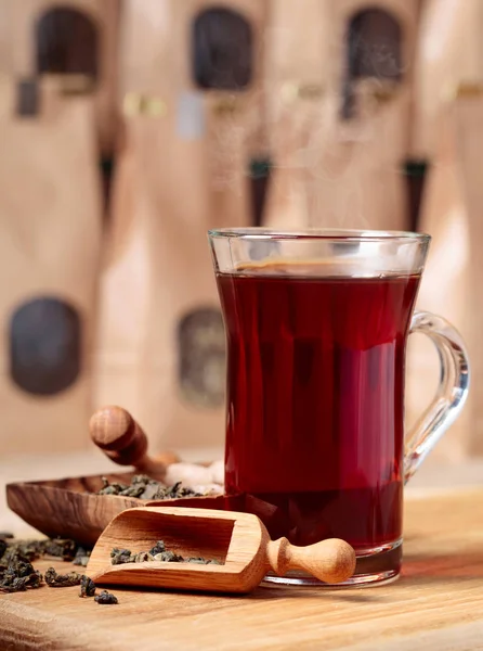 Verre de thé chaud et cuillère en bois avec des feuilles de thé séchées . — Photo