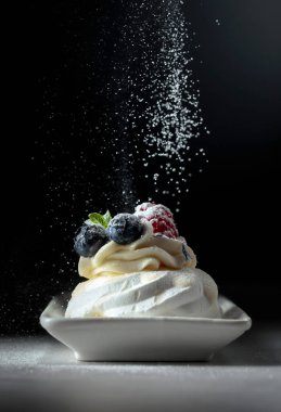 Tatlı Pavlova ile pudra şekeri serpilir.