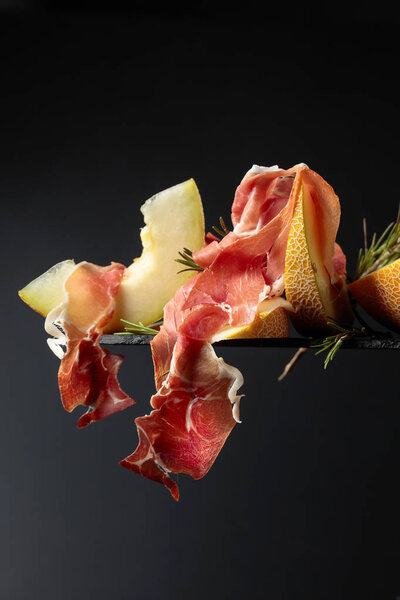 Prosciutto with melon and rosemary  on a black background.