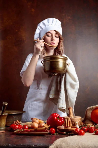 Jeune femme en uniforme de chef avec vieille casserole en laiton et spo en bois — Photo