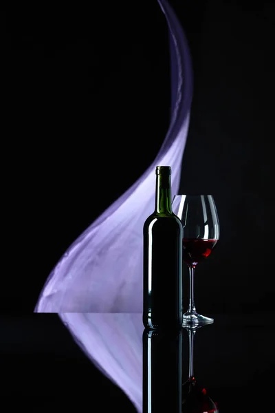 Weinglas und Flasche Rotwein auf schwarzem reflektierendem Hintergrund — Stockfoto
