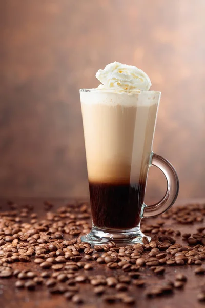 Glasbägare med kaffe och kaffebönor på brun bakgrund. — Stockfoto