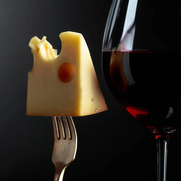 Queijo Maasdam com vinho tinto sobre fundo preto . — Fotografia de Stock