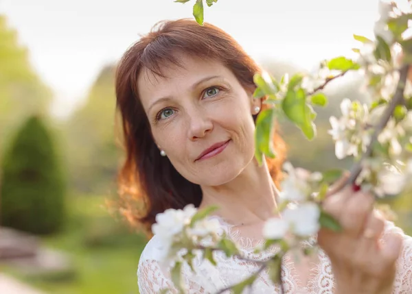 Attraktive Brünette in einem weißen Kleid neben einem blühenden Apfelbaum — Stockfoto