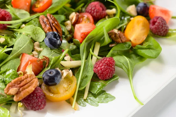 Green salad with raspberry, strawberry, blueberry and nuts.