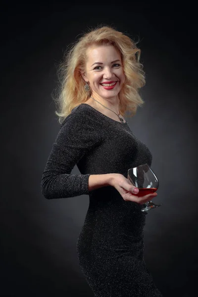 Attraktiv leende kvinna i svart aftonklänning med liten drink o — Stockfoto