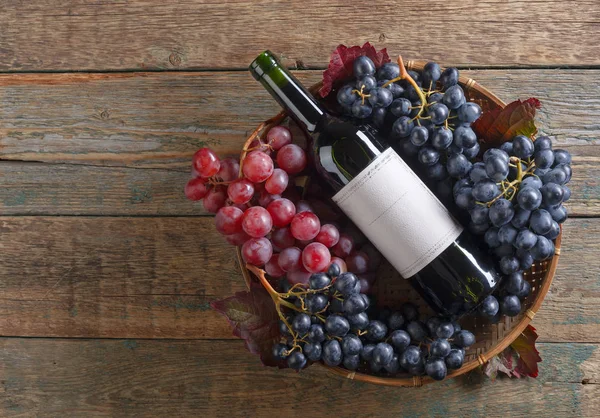Виноград і пляшка червоного вина на старому дерев'яному столі . — стокове фото
